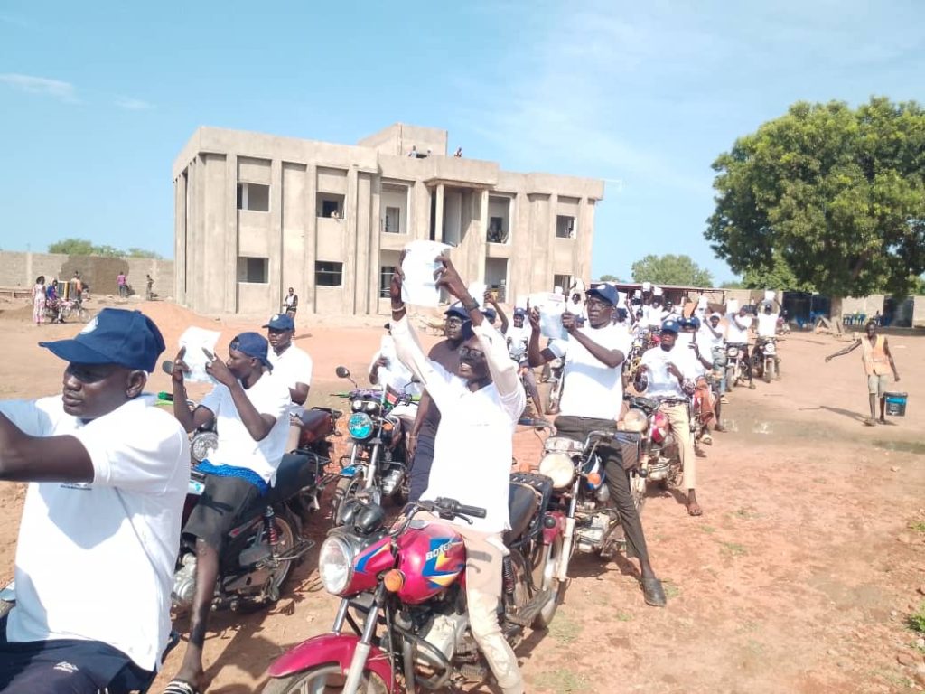 Motorcycle riders carry campaign materials through Kuajok